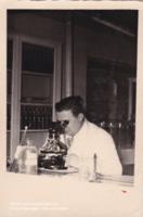 Joris van Gheluwe in een witte stofjas aan het werk met een microscoop. 