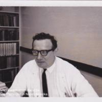 Portretfoto van Joris Van Gheluwe in witte stofjas aan een bureau